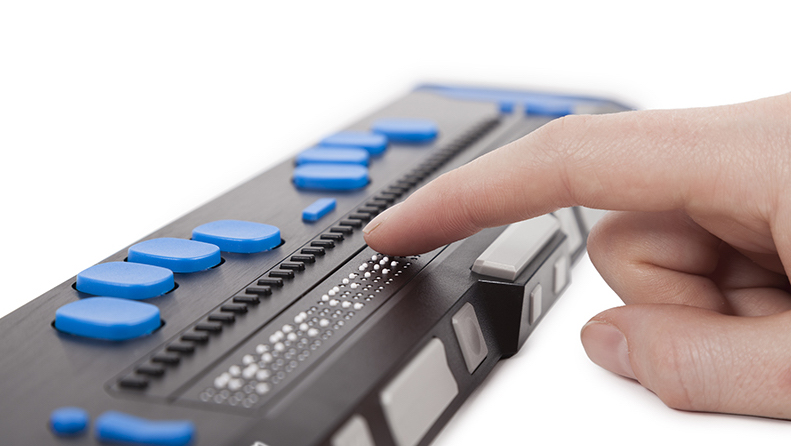 A close-up of a hand hovering over a refreshable braille display's output.