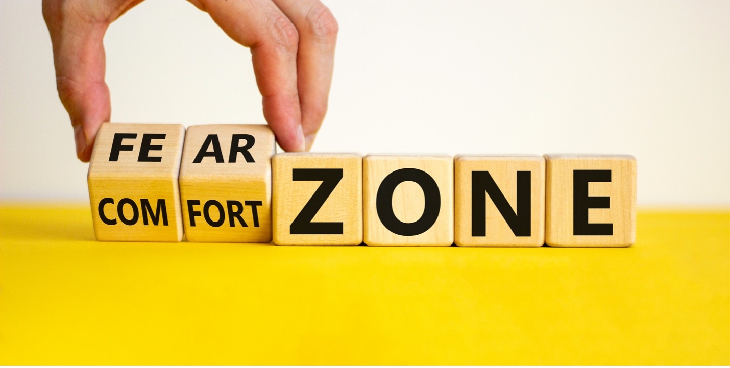 A hand rotating two wooden blocks that line up with four static blocks. The blocks have letters on them spelling out [FE-AR]-Z-O-N-E and [COM-FORT]-Z-O-N-E respectively. All are on a solid yellow surface.