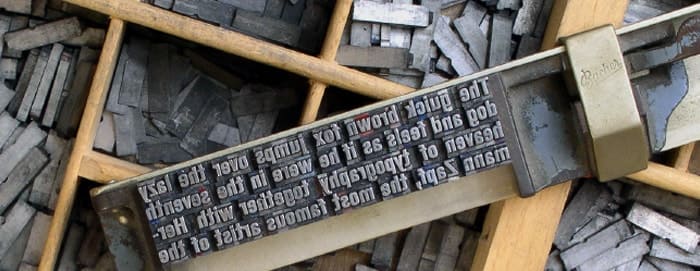 A picture of words being set to print in a 15th century printing press. The text "The quick brown fox jumps over the lazy dog and feels as if he were in the seventh heaven of typography together with Hermann Zaqf, the most famous artist of the" is set backwards ready to press, and it rests on wooden compartments full of letters available to set.