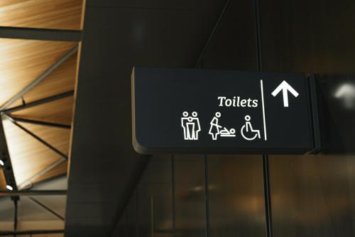 A picture of a sign indicating where the accessible toilets are. On the left is the word toilets with stick figures of a family, then a parent changing a child's diaper, then a person in a wheelchair. On the right is an arrow indicating that the toilets are ahead.
